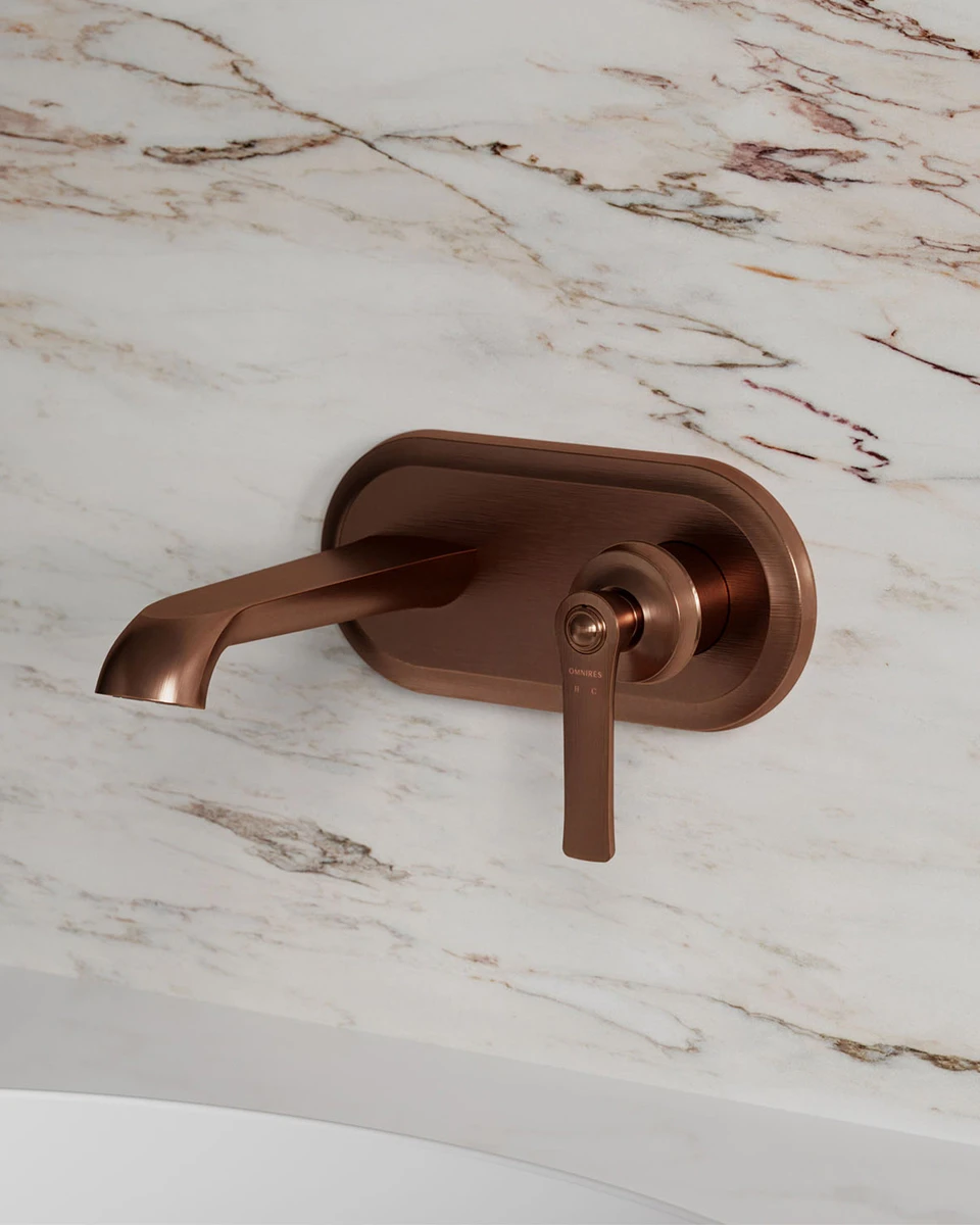 ARMANCE wall-mounted basin mixer in a copper finish against marble